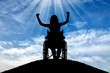 Silhouette of a happy disabled woman in a wheelchair on top of a hill