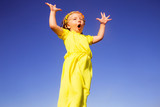 Fototapeta  - A little girl stands at the top of a haystack, raises her hands