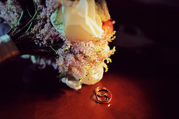 Wedding rings, jewelry and symbols attributes taken with selective focus. Holiday, celebration. Macro. Blur. Bridal bouquet on background