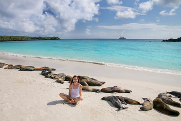 Wall Mural - Young woman sitting with a group of Galapagos sea lions at Gardner Bay, Espanola Island, Galapagos National park, Ecuador