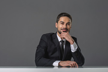 Waist up portrait of cheerful bearded man. He is sitting at the table with chin propped in hand and holding smartphone. Copy space in left side