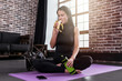 © undrey - Portrait of young caucasian woman resting after training holding a sports bottle sitting on mat with legs crossed in gym with loft interior