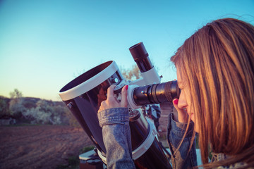 Wall Mural - cute young woman holding astronomical telescope and looking at the sky.