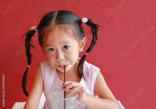 Photo Close up little girl using straw to drink water from plastic cup in the restaurant