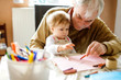 © Irina Schmidt - Cute little baby toddler girl and handsome senior grandfather painting with colorful pencils at home. Grandchild and man having fun together