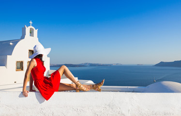 Santorini travel tourist brunette woman in red dress visiting famous white Oia village.