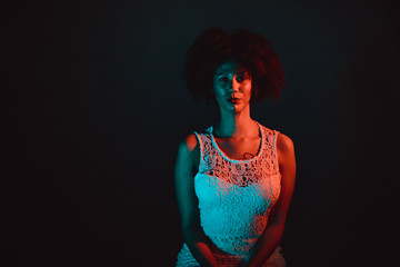 Wall Mural - Beautiful black woman with curly hair showing her naked back, wearing a white dress in a studio in front of a dark background