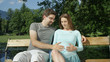 © helivideo - CLOSE UP: Relaxed parents to be sitting on a sunlit bench caressing baby bump