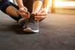 © oatawa - Woman tying running shoes on black floor background in gym with sunlight. copy space.