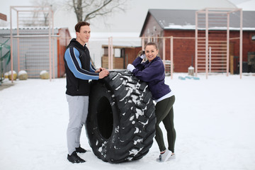 Wall Mural - Young sporty woman and man with heavy tire, outdoors