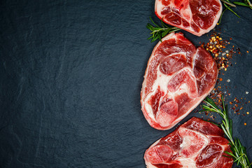 Raw juicy meat steaks ready for roasting and vegatables on a black board background. Space for text