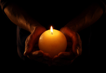 Wall Mural - Young man holding burning candle in darkness