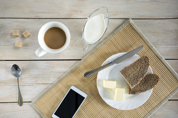 White smartphone,  a cup of coffee and bread with butter on wooden table