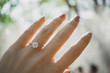 Close up of an elegant diamond ring on woman finger with blurry forest and sunlight background. soft and selective focus. Love and wedding concept.