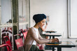 Portrait of a slim, young Muslim Malay woman sitting and working at a cafe during the day. She is wearing a turban and is fashionably dressed.