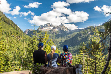 Father, mother and daughter is sitting in from of the scenic view where clouds are covering snowy mountain summits in the middle of the green sunny forest