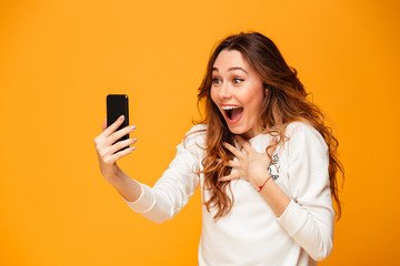 Canvas Print - Surprised brunette woman in sweater using smartphone while rejoices