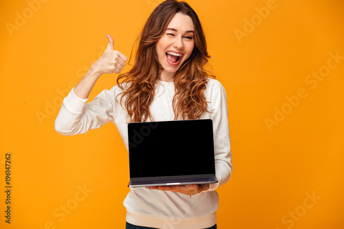 Cuadros en Lienzo Cheerful brunette woman in sweater showing blank laptop computer screen
