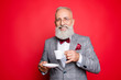 © deagreez - Portrait of cool, manly, elegant, fashionable man looking at camera, having mug with tea and saucer in arms, isolated on red background