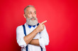 © deagreez - Portrait with copy space of minded, ponder, professional, retro stylist, barber with blue bowtie and suspenders pointing on empty place, product with forefinger, isolated on red background