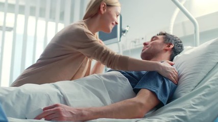 Wall Mural - In the Hospital, Happy Wife Visits Her Recovering Husband who is Lying on the Bed. They Lovingly Embrace and Smile. Shot on RED EPIC-W 8K Helium Cinema Camera.