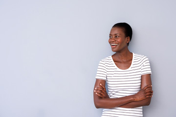 Wall Mural - happy young african lady with arms crossed looking away and smiling on gray background