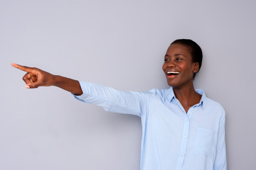 Wall Mural - happy young african woman pointing away with finger on gray background