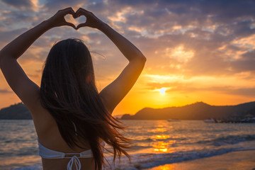 Wall Mural - Woman with bikini making heart sign on beach