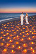 Loving couple at tropical sunset ocean sandy beach with lot of candles lights. Proposal, wedding, valentines day or honeymoon vertical background concept.