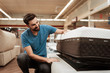 Young bearded man is testing mattress in furniture store. Orthopedic mattress for a healthy posture.