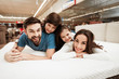 Little children lie on the backs of young happy parents in a mattress store.