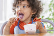 Toddler sitting in highchair and eating greek yogurt. Baby learning to eat and has yogurt on face and hair