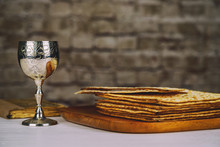 Red Kosher Wine With A White Plate Of Matzah Or Matza And A Passover Haggadah On A Vintage Wood Background Presented As A Passover Seder Meal With Copy Space.