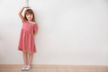 Cute little girl measuring height near light wall