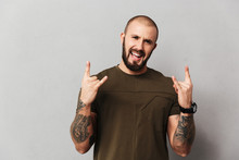 Image Of Cheerful Hairless Guy With Beard And Mustache Smiling And Showing Rock Sign, Isolated Over Gray Background