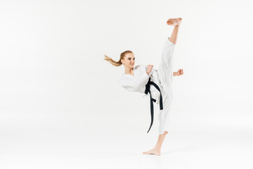 Female karate fighter with black belt performing kick isolated on white