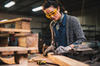 © dusanpetkovic1 - Professional carpenter woman sanding and preparing wood at the table in the fabric workshop.