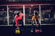 © Dusan Petkovic - Young attractive sporty inspired woman bending over doing kettlebell exercises with a personal trainer in front of gym mirrors.