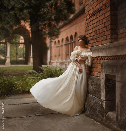 A young lady stands at the wall of an ancient castle looking with hope in the distance. Emotion waiting for the long-awaited. A white vintage dress flutters in the wind. Artistic Photography