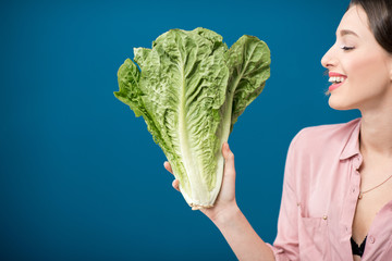 Wall Mural - Woman holding a green lettuce on the blue wall background