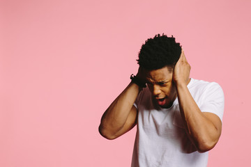 Wall Mural - Portrait of a young man in white shirt holding his head in distress, on pink background