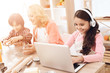 © freeograph - Joyful girl in headphones sits behind laptop next to her grandmother and brother watching tablet in kitchen.