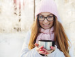 © mak_alexandra - Adorable happy young blonde in pink knitted hat scarf holding a hot mug sitting in a snowy winter forest