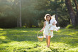 Little girl walking barefoot toward camera, holding Easter basket with eggs and plush toy big bunny