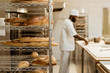 © LIGHTFIELD STUDIOS - african american baker preparing raw dough at workplace with shelves of fresh loaves of bread on foreground
