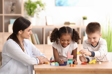 Wall Mural - Young woman playing with little kids indoors. Child adoption