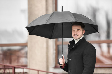 Poster - Young man in warm clothes with dark umbrella outdoors