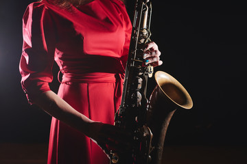 Musician girl in a red dress with a saxophone on stage