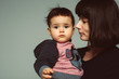 Profile of young mother with dark short hair holding her son toddler, serious sad child with chubby cheeks, looking at camera, isolated in studio, space for text