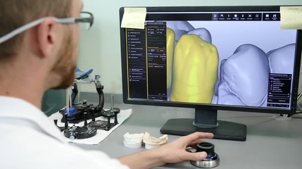 digital diagnosis of teeth, dentist looks at computer screen with stickers sitting at desk with artificial jaw indoors, side view